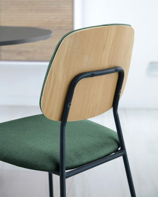 Cadeira Empilhável Benilda Verde com assento em tecido chenille e encosto revestido em carvalho natural. Estrutura de metal com acabamento pintado preto mate. Equilíbrio entre estilo retro e contemporâneo.